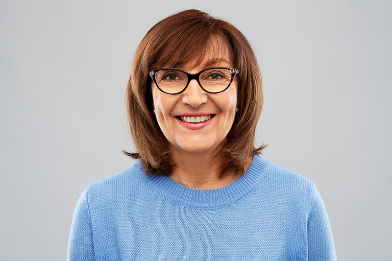 Odmładzające fryzury - uśmiechnięta kobieta w wieku około 60 lat. Piękne brązowe włosy z grzywką.